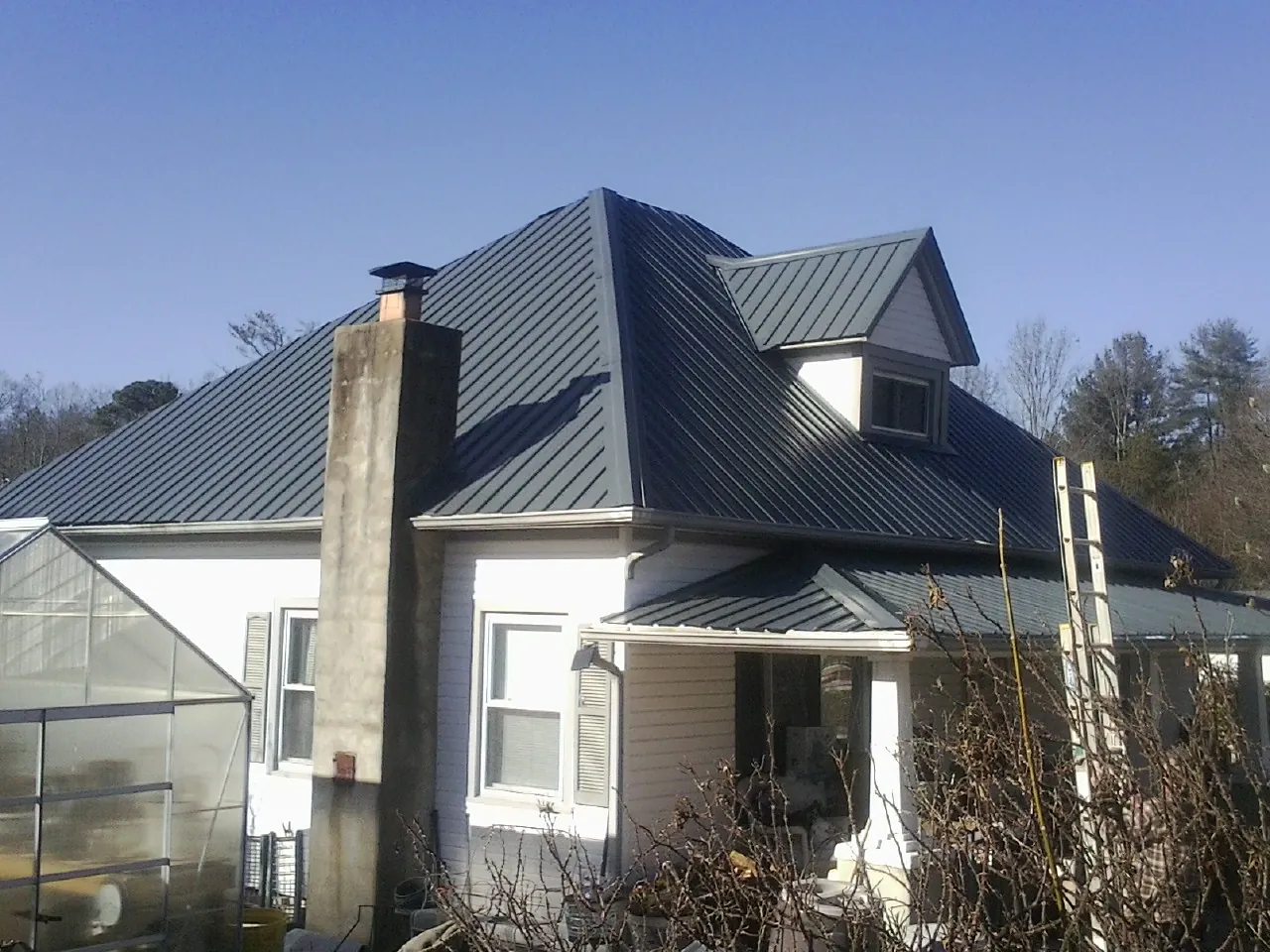 Dark blue standing seam metal roof on a white farmhouse with dormer — Slate & Tile Roof Repair by Roofing Brothers in Aspen