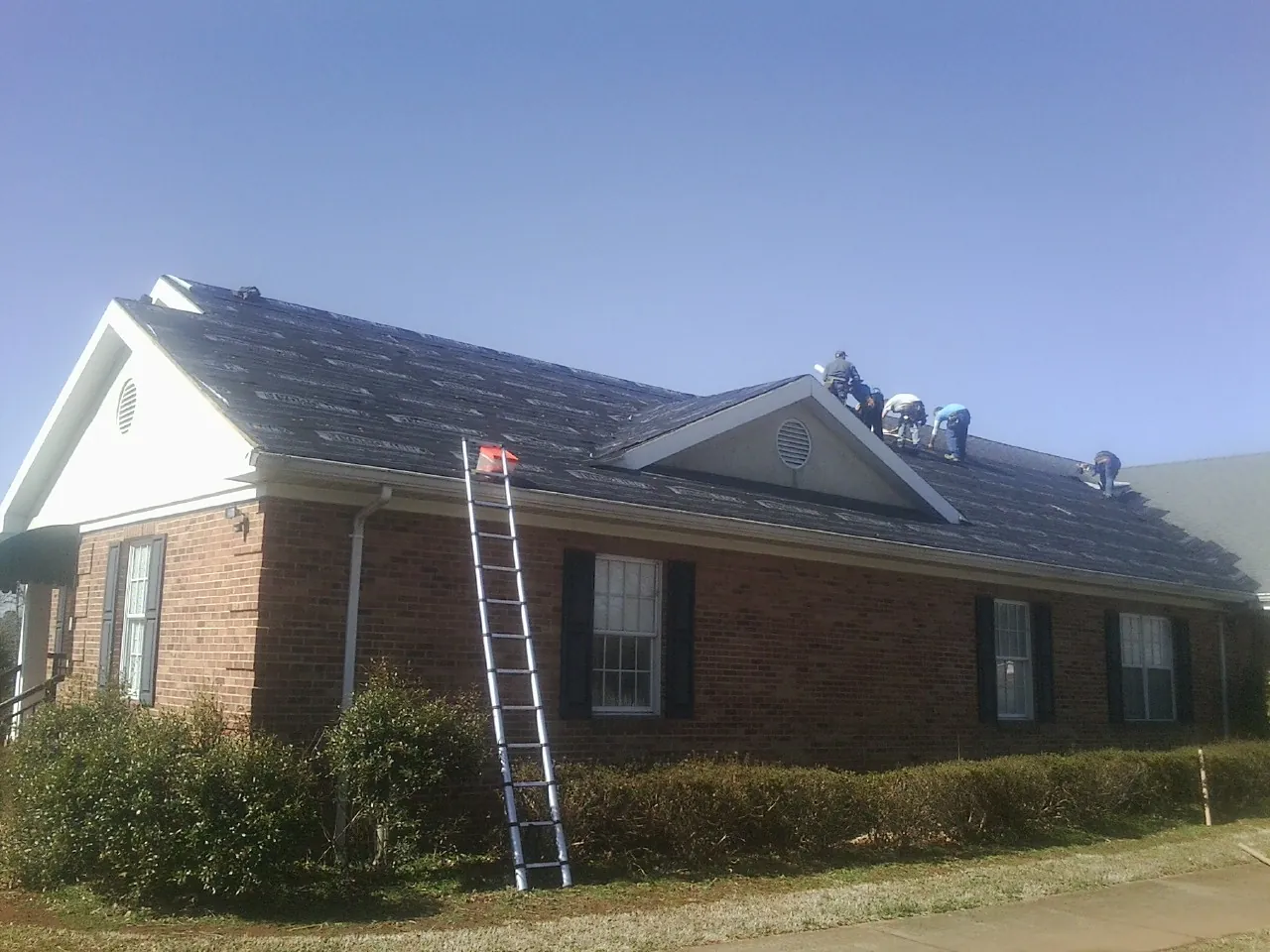 Crew tearing shingles off a brick ranch roof with a ladder set — Metal Roof Repair work by our crew in Aspen