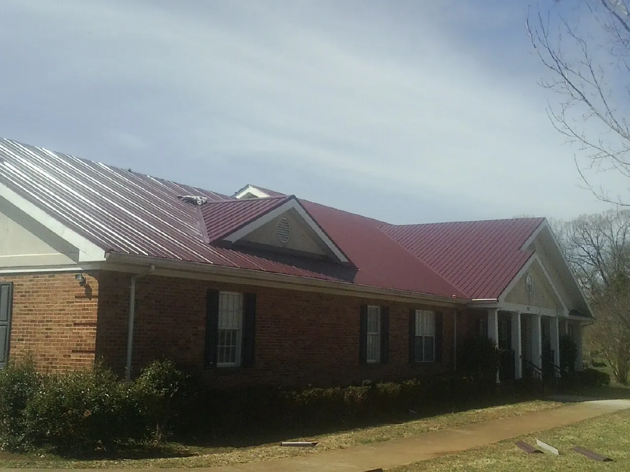 Red metal roof with gabled entries on a long brick building, from a Hail Damage Roof Repair job in Aspen