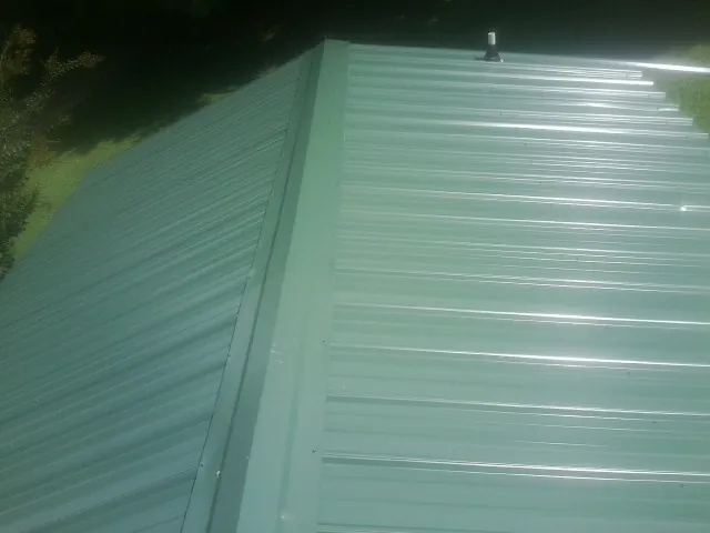 New green metal panels meeting at the ridge of a roof — Flat Roof Repair work by our crew in Aspen