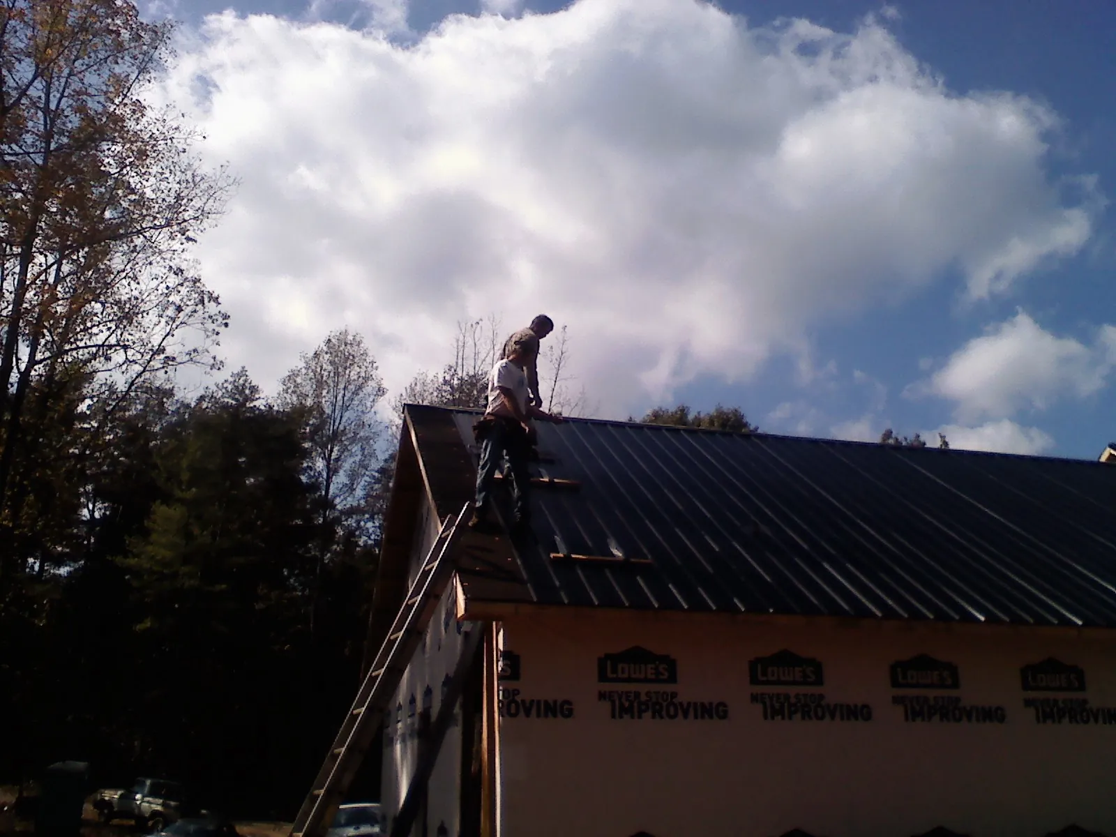Roofer fastening dark metal panels high against a cloudy sky, from a Roof Inspection job in Aspen